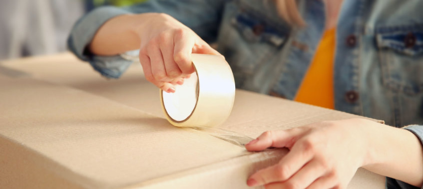 Young girl sealing with tape big cardboard box for moving